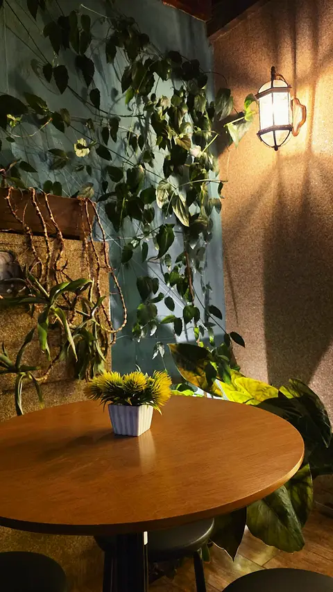 Mesinha redonda na varanda, com vaso de flor e folhagem na parede